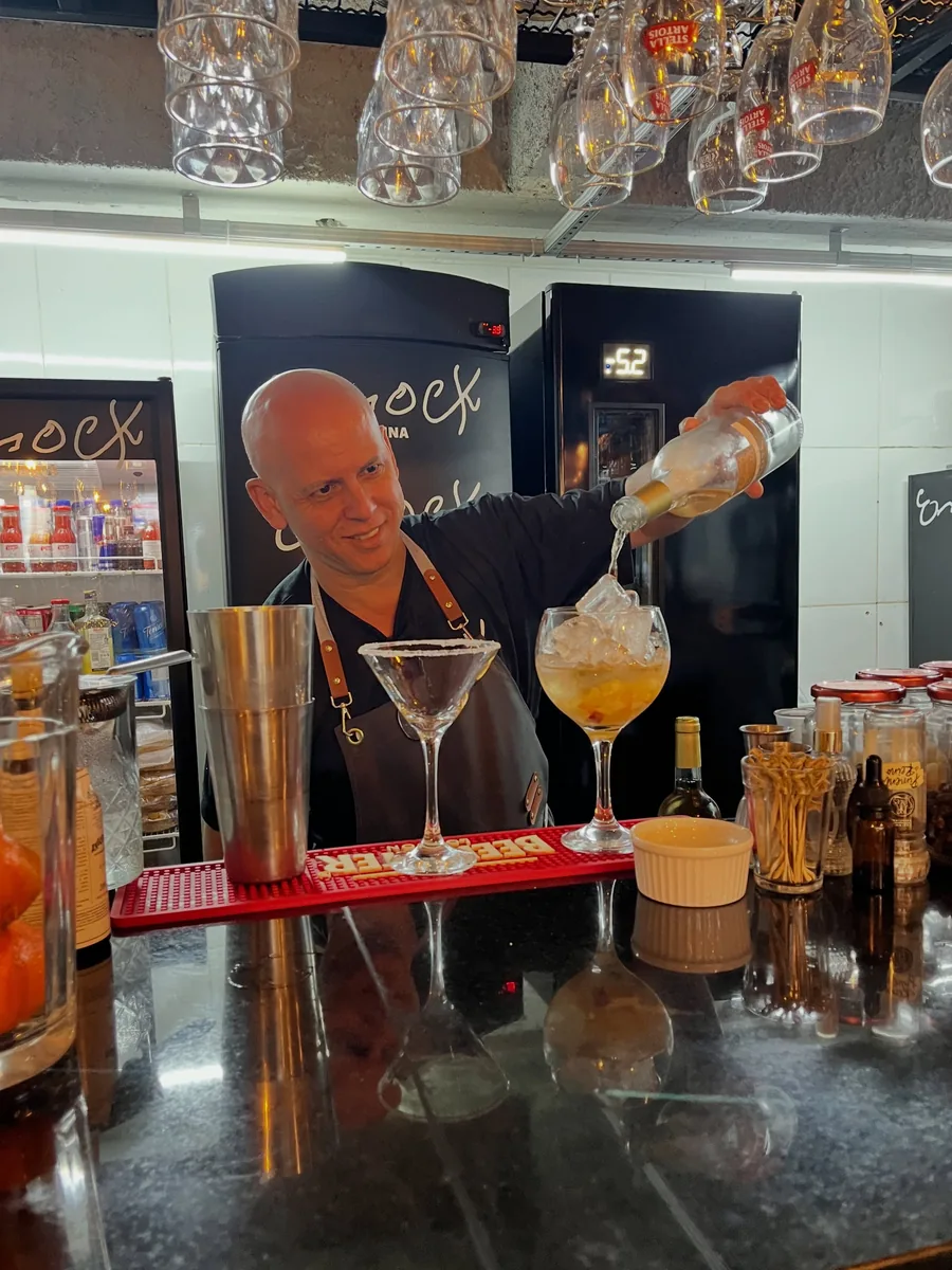 Empregado de balcão a servir um cocktail vermelho, com as garrafas da casa em fundo