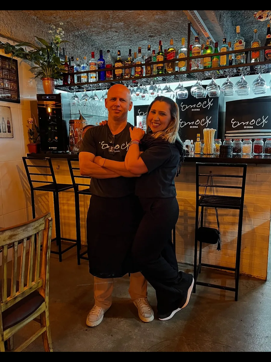 Duas pessoas da equipe do Enock di Dina atrás do balcão, ao fim do serviço