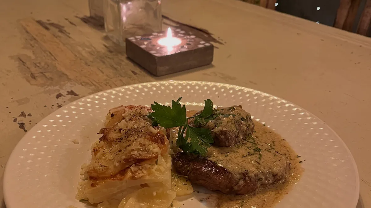 Prato gratinado servido na mesa, com a lamparina acesa ao lado