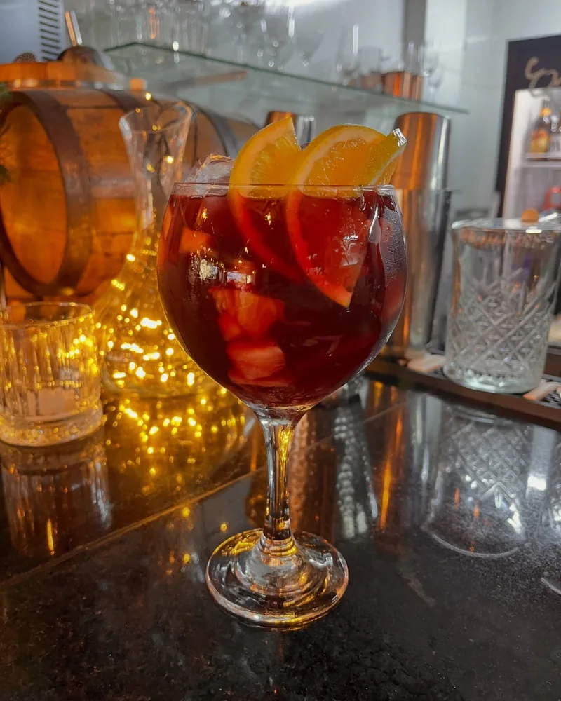 Taça de sangria com laranja e gelo, servida no balcão iluminado